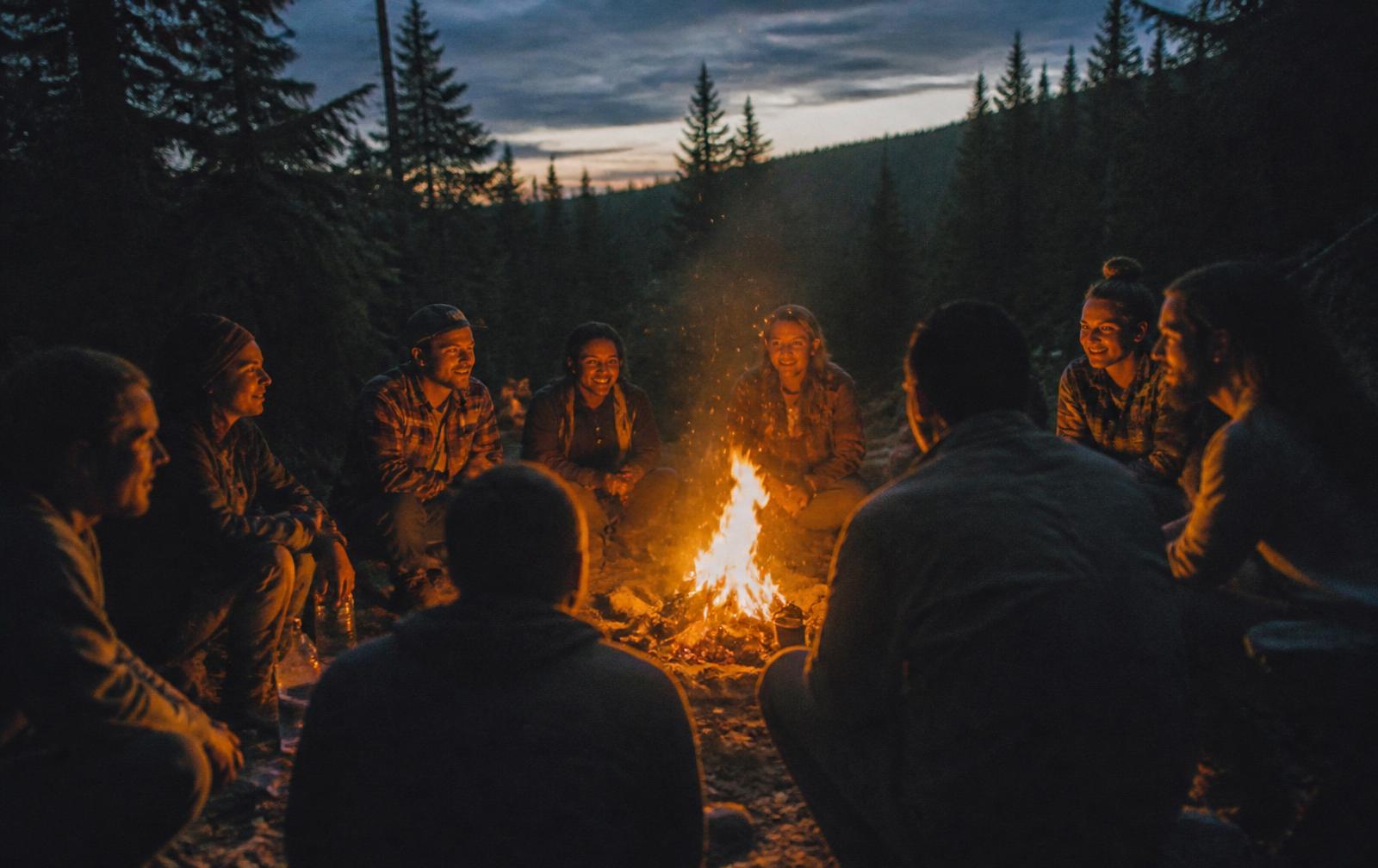 A circle of people gathered around a campfire at dusk